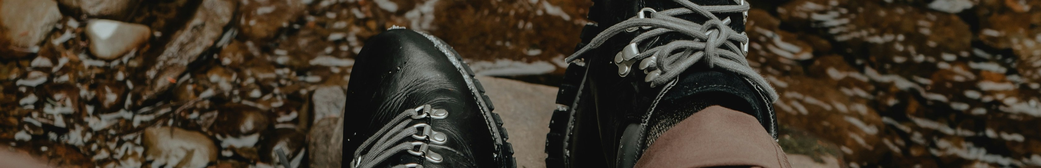 Homme portant des bottes noires assis devant un ruisseau.