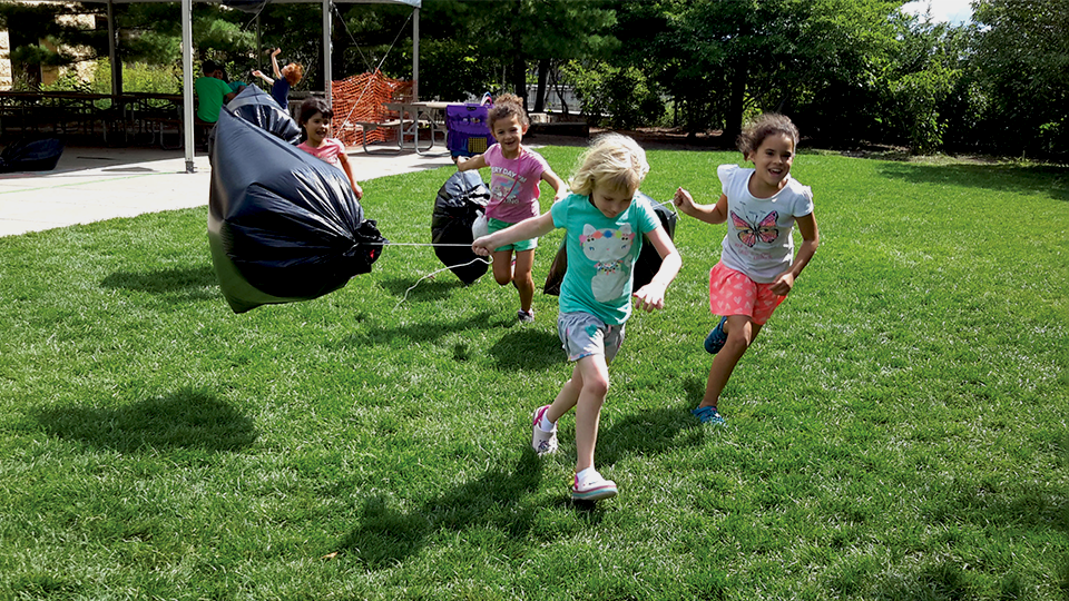 A photo of children running outside at the Science Museum of Minnesota with self-made kites.