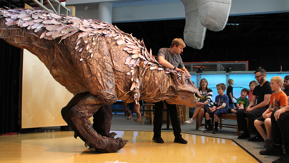 A T.rex puppet interacts with an audience in the museum.