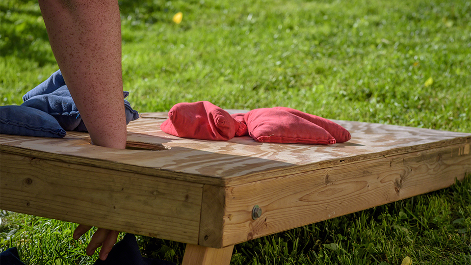 person reaching for bean bag in cornhole