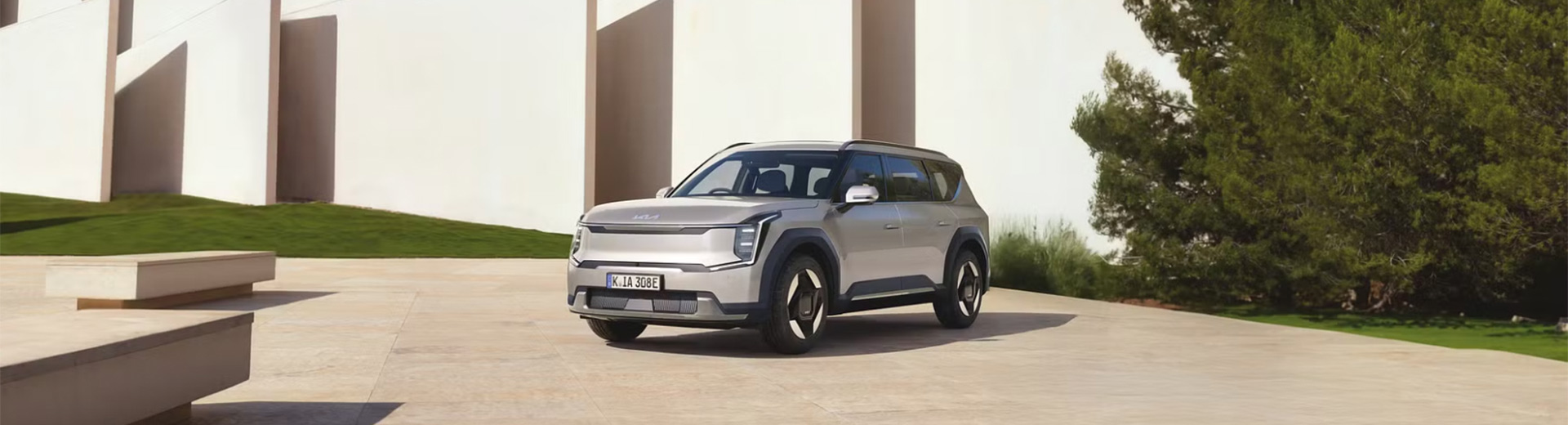 En-silverfärgad-Kia-EV9-parkerad-framför-en-modern-vit-byggnad-i-solljus