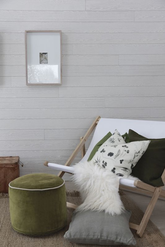 Minimalistisk hjørne: lys trestol med hvitt lerret, pelskinn, grønne puter og puf mot grå trevegg