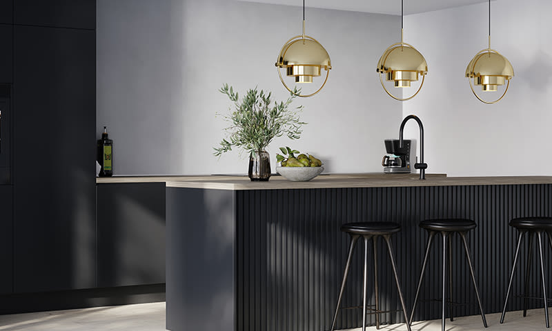 Svart kjøkkenøy med tre gullpendler, barstoler, kaffetrakter, vase med kvister og frukt