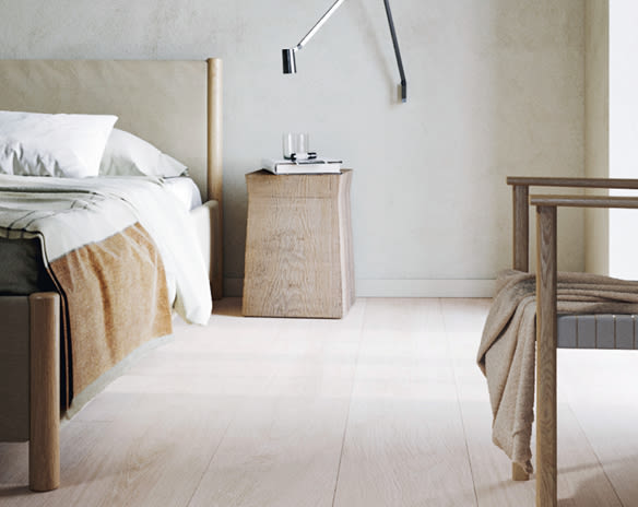 Stilrent soverom i lyst tre, hvit seng med okergult pledd, trebord og vegglampe.