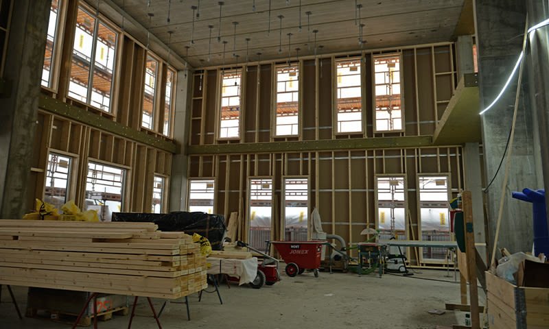 Rom under oppføring med åpne trekonstruksjoner, stabel med bjelker, høyt tak og store vinduer