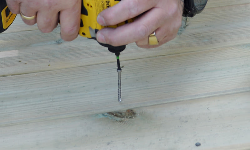 Nærbilde av hender med gul drill som skrur inn skrue i lyst treverk