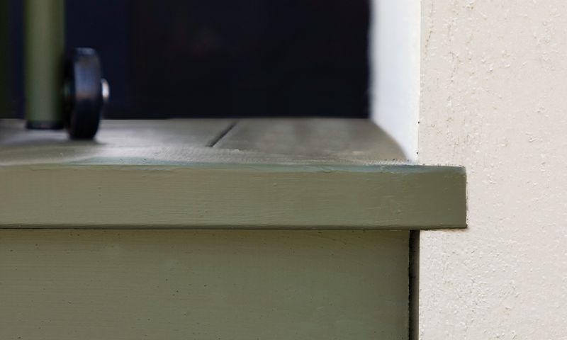 Grønnmalt vinduskarm mot hvit vegg, med et lite svart hjul på venstre side.