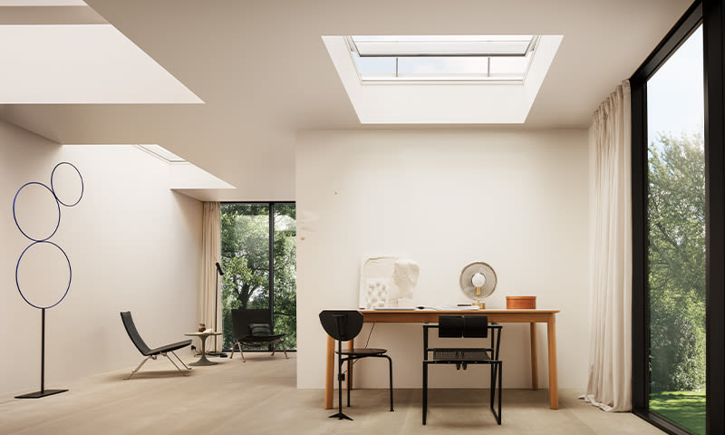 Lyst, minimalistisk rom med skrivebord i tre, svarte stoler, takvindu og hageutsikt.