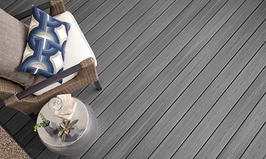 Rottingstol med hvit pute og blå mønstret pute; sidebord med glass, bok og plante på grå terrasse