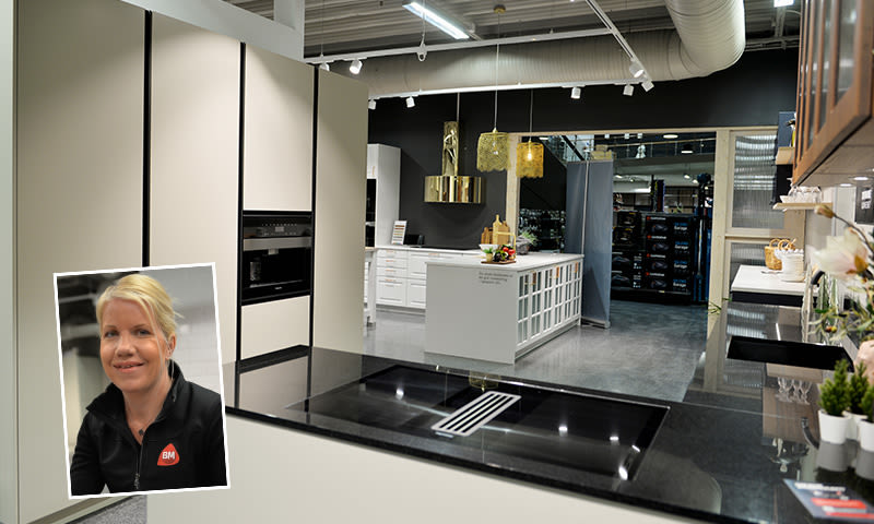 Moderne kjøkkenutstilling i butikk med lys kremfronter, sort benkeplate, hvit øy og gullpendler