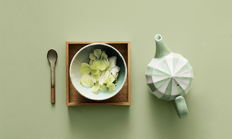 Oversiktsbilde av grønn-hvit tekanne, skål med lysegrønne hortensiablomster på trefat og treskje