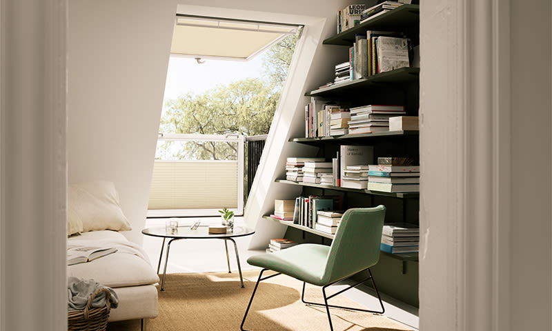 Lys lesekrok på loft med grønn stol, rundt bord, beige sofa og mørkegrønn bokhylle ved vindu