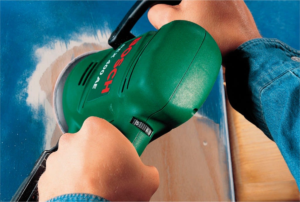 Hender i blå skjorte sliper blåmalt treflate med grønn Bosch slipemaskin.