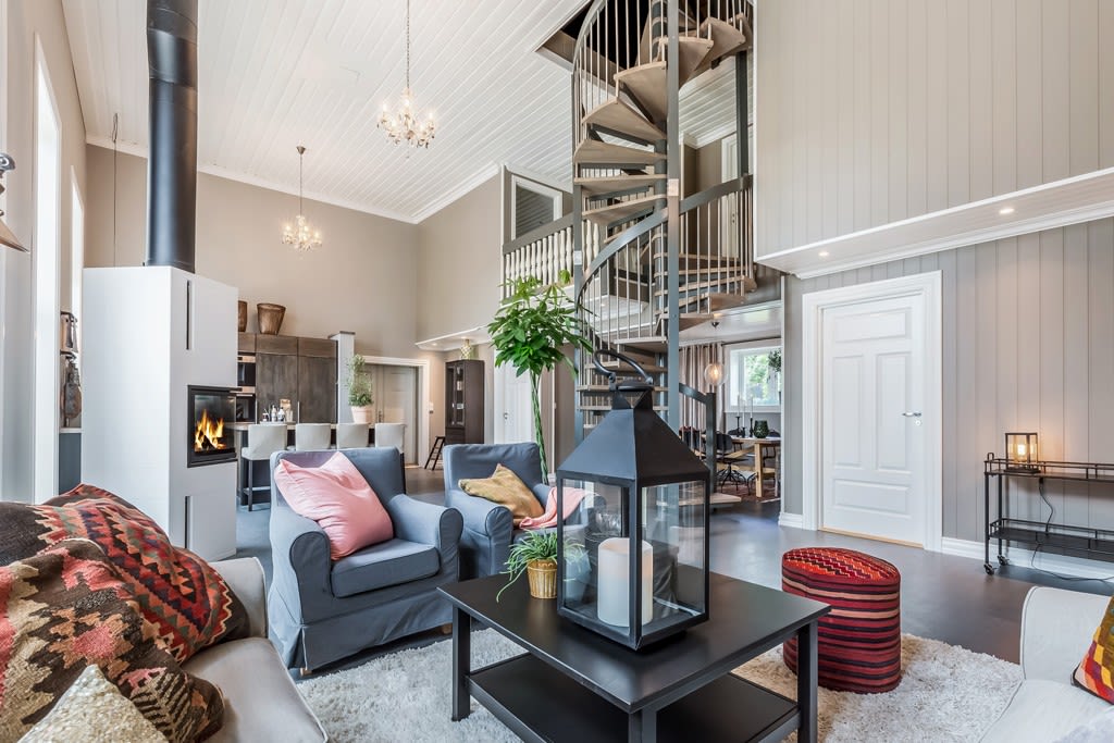 Lys, åpen stue med grå møbler, hvit peis, svart spiraltrapp og rosa puter.