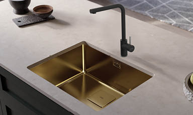 Gullfarget nedsenket kjøkkenvask med matt svart kran på lys beige benkeplate.