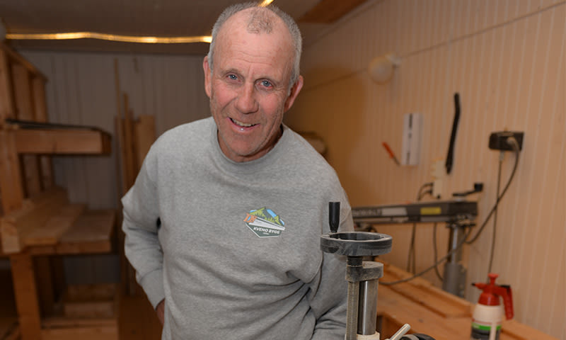 Mann i grå genser i lyst treverksted med stor skrustikke festet til arbeidsbenk