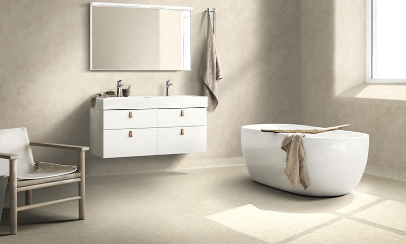 Moderne lyst baderom med beige vegger, hvit dobbel vask m/speil, frittstående badekar og lenestol.