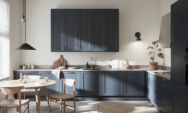 Moderne kjøkken med mørkeblå skap, lys benkeplate, rundt trebord, hengelampe og grønn plante.