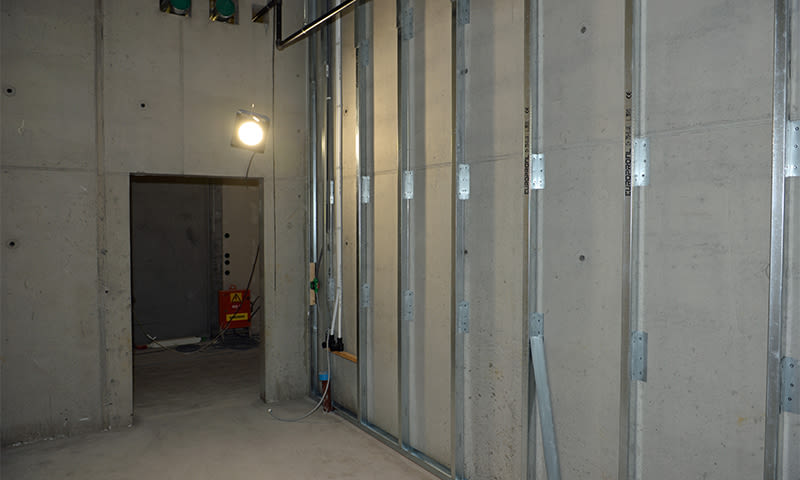 Uferdig rom med grå betongvegger, metallstendere, arbeidslys og elektriske kabler