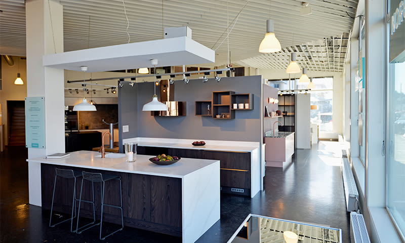 Moderne kjøkkenutstilling med hvite benkeplater, mørke treskap, grå vegg og pendellamper.