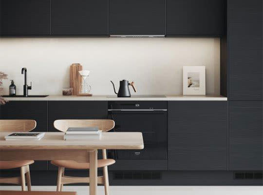 Moderne kjøkken med svarte skap, hvit benkeplate, trebord, kaffekjele og ramme.