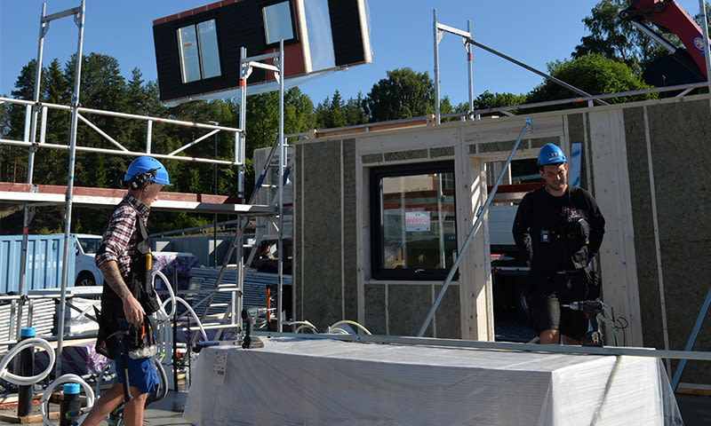 Arbeidere i blå hjelmer ved modulhus under montering på solrik byggeplass.