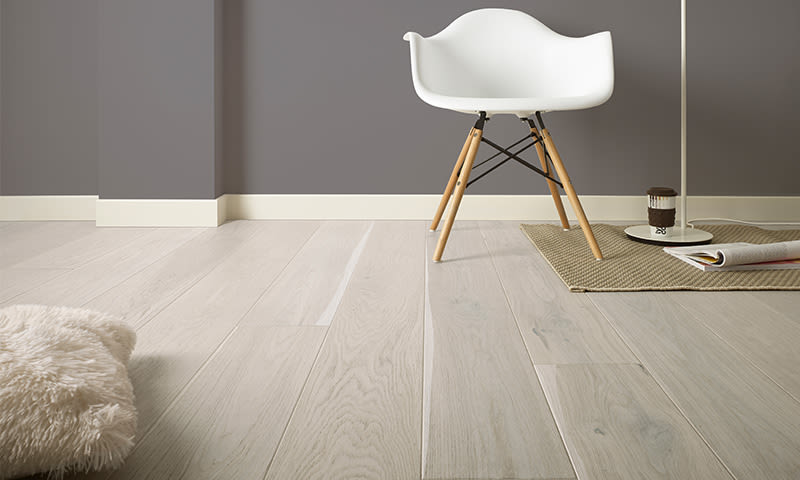 Minimalistisk interiør: lys eikegulv, grå vegg, hvit stol, gulvlampe, teppe med kaffekopp.