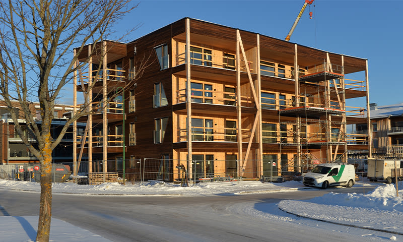 Trebygg under oppføring med stillas, kran, snø og hvit-grønn varebil.
