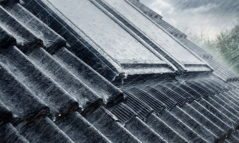 Vinklet nærbilde av mørke grå takstein i kraftig regnvær