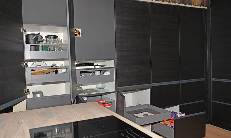 Moderne kjøkken med mørke skap og skuffer, åpne hyller med gryter, glass og redskaper.
