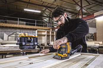 Person pusser treplate med gul-svart el-sander i stort lyst verksted