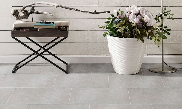 Sort metallbenk med bøker og drivved ved siden av hvit vase med rosa magnoliablomster, grå fliser