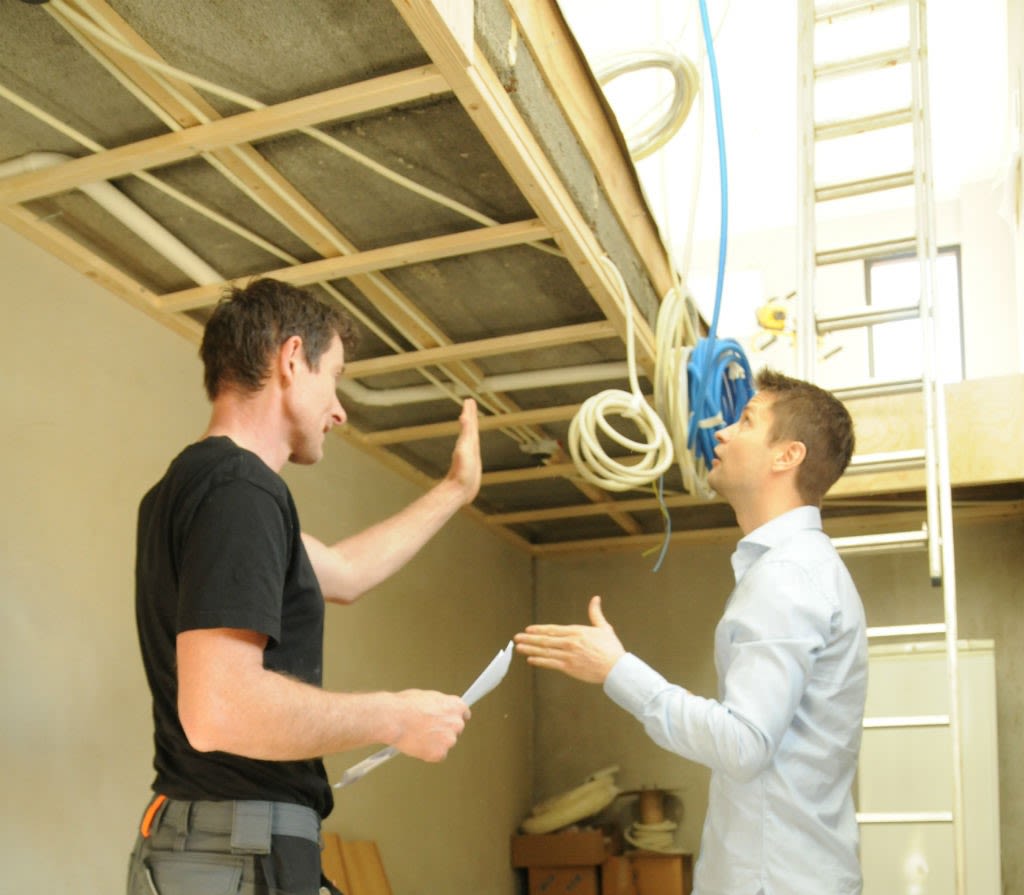 To menn i oppussingsrom peker på åpen takramme med elektriske kabler og stige.