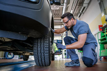 Mekaniker i blå arbeidsklær bruker muttertrekker på bilhjul i lyst verksted.