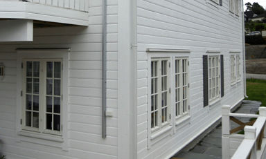 Hvit trevilla med panelet fasade, flere hvite sprossevinduer og lav veranda i rolig boligområde