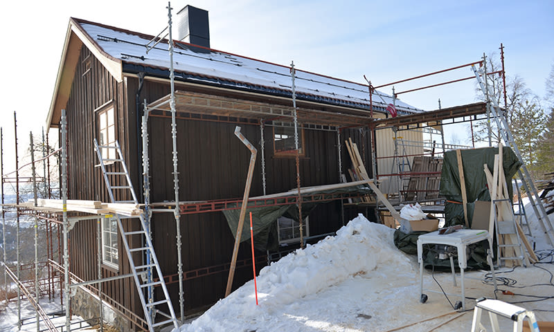 Brun hytte i snø med stillas, stiger og byggeutstyr under vinteroppussing.