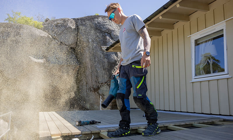 mann bruker løvblåser for å rydde opp i byggeplass på terrassen