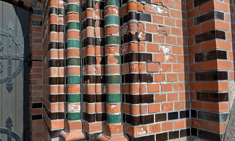 Nærbilde av rødoransje mursteinsvegger med glaserte grønne og svarte søyler ved port