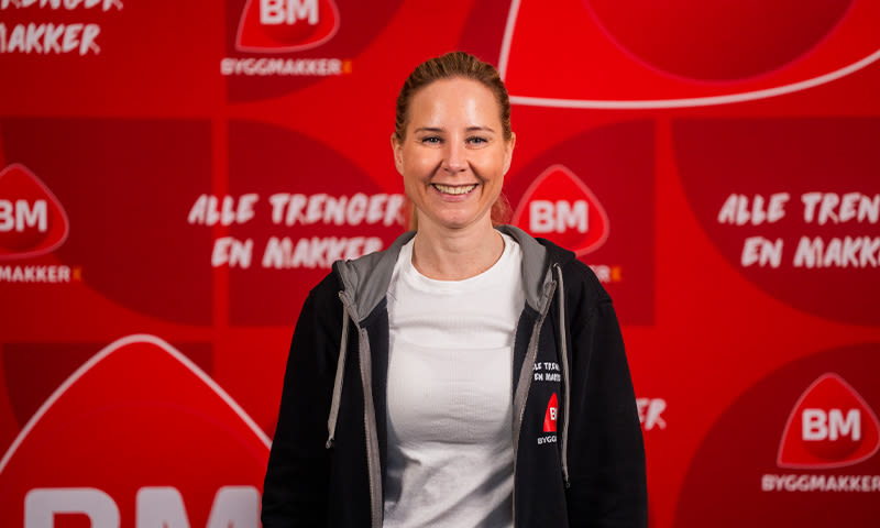 Person i hvit T-skjorte og svart hettegenser med BM-logo foran rød reklamevegg