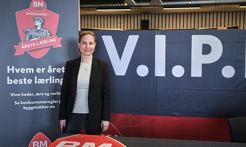 Person i dress foran rød-hvitt Byggmakker Årets lærling-banner og svart V.I.P.-plakat