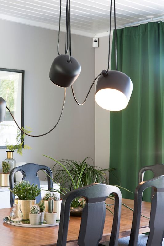 Spisebord i tre med kaktusplanter på sølvfat, hengende sorte lamper foran grønn gardin.