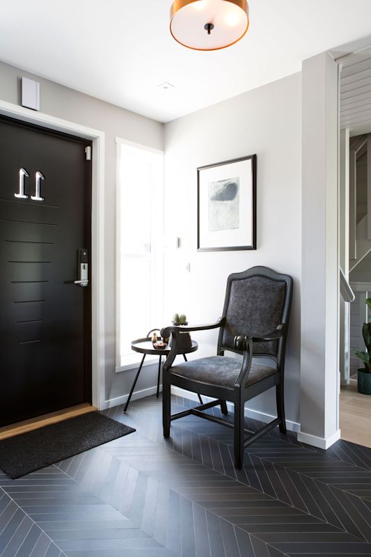 Lyst inngangsparti med svart dør nr. 11, grå stol ved vindu, bord med kaktus og abstrakt kunst