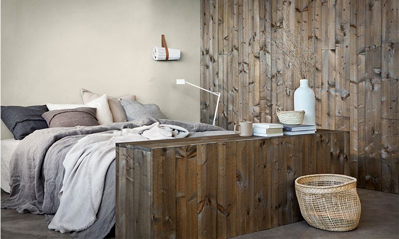 Lyst soverom med stor seng, grått sengetøy og trefinerte veggpaneler, kurv og vaser.