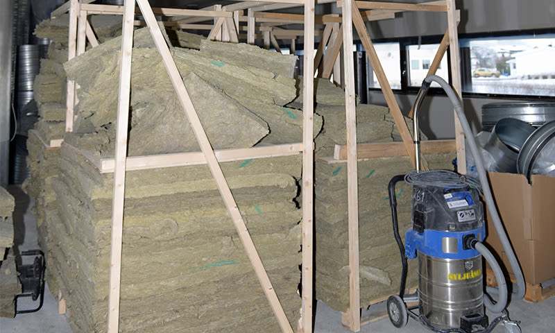 Stabel av grønne isolasjonsplater i trestativ ved blå-sølv industristøvsuger i byggeinteriør