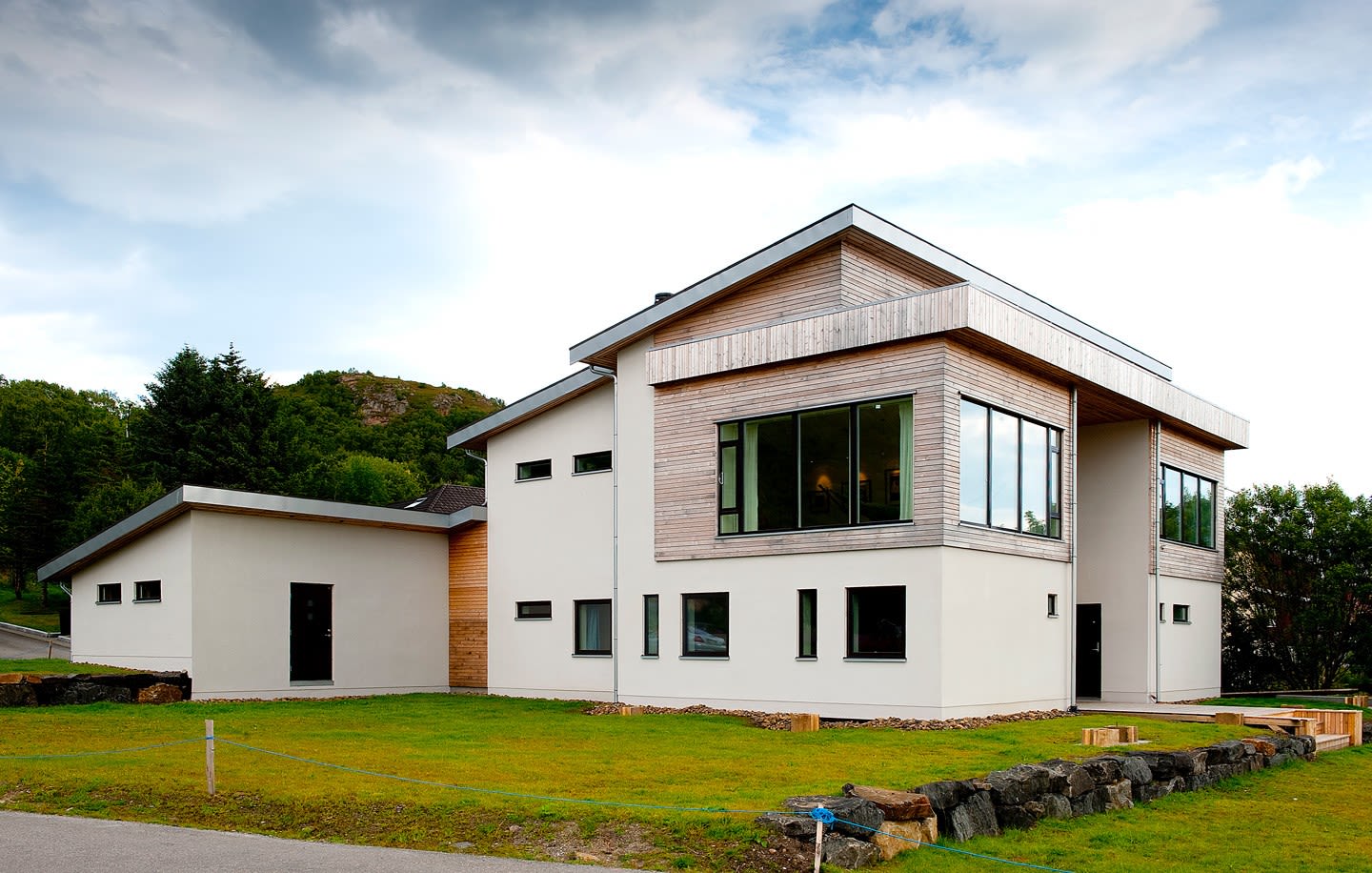 Moderne hvit og trefasade enebolig med store vinduer, grønn plen og trær i bakgrunn