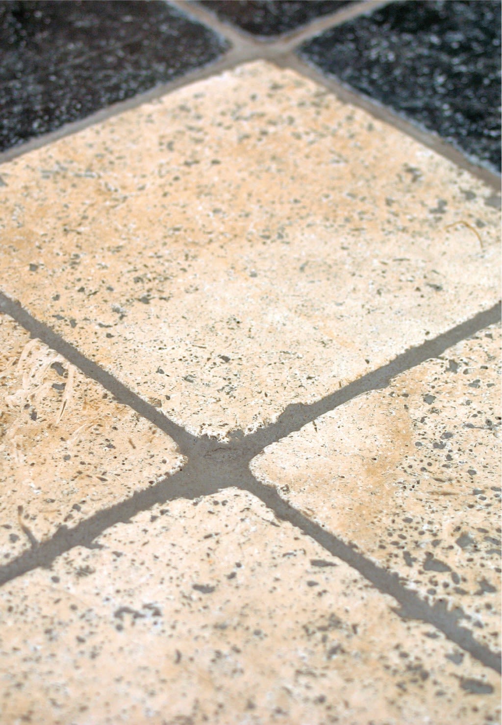 Nærbilde av diagonalt plasserte krem- og svarte fliser med mørk grå fugemasse