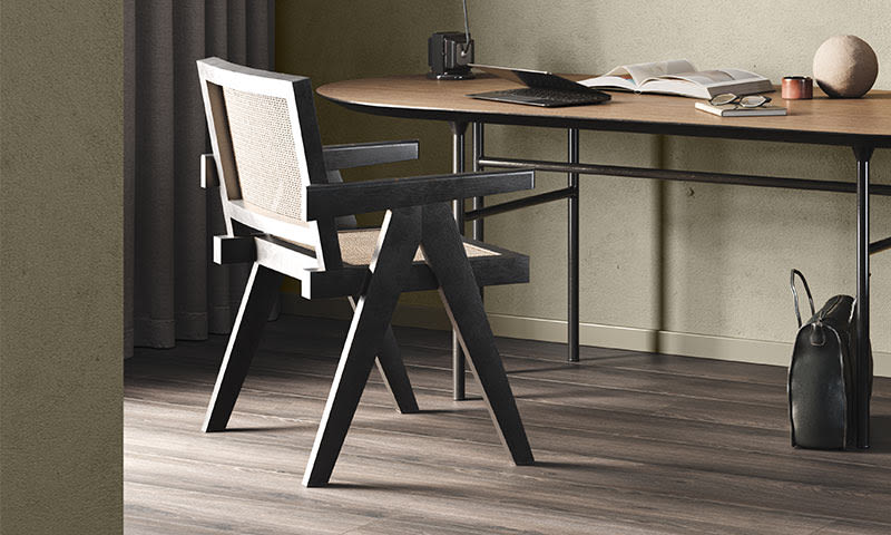 Lyst hjemmekontor med mørk grå trebokstol, lyst trebord, laptop, åpne bøker og svart veske.