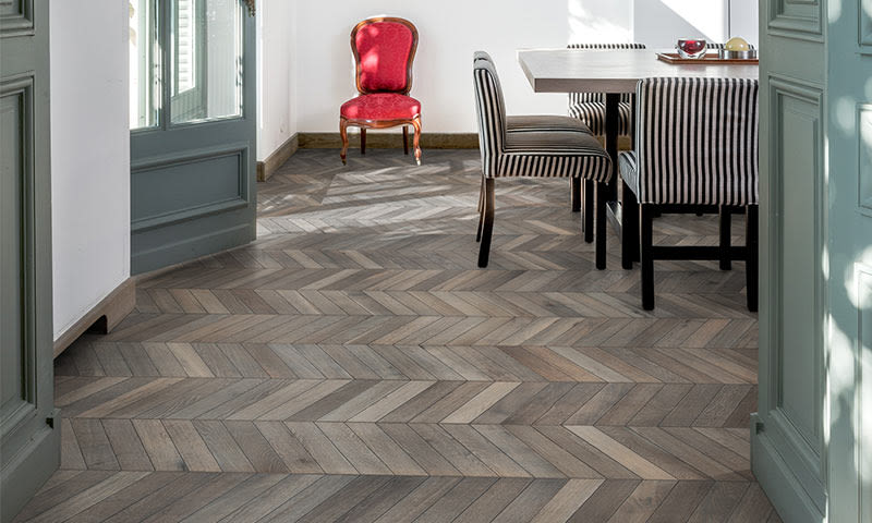 Lyst rom med grå fiskebeinparkett, rødt antikkstol ved hvit vegg og stripete spisestoler.