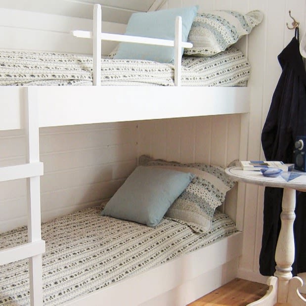 Hvit trebunkerseng med blå-hvite mønstrede sengeklær, lyseblå puter og rundt sidebord.