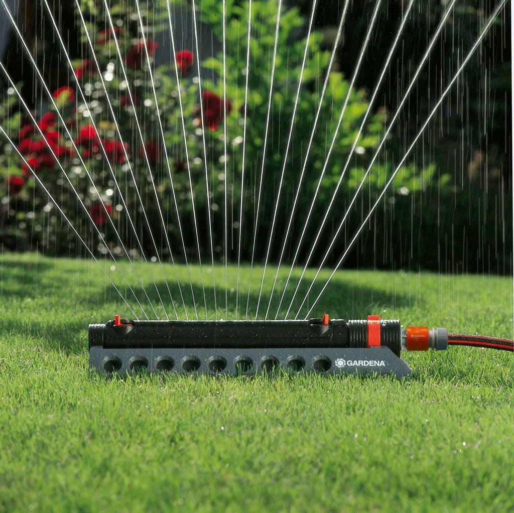 Sort Gardena-oscillerende sprinkler med rød kobling på grønt gress sprayer vann i vifte